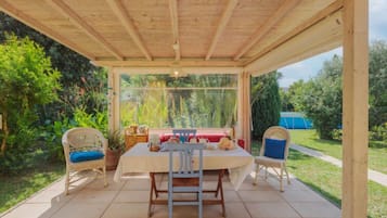 Une terrasse couverte avec une table et des chaises, entourée de verdure et offrant une vue sur un jardin.