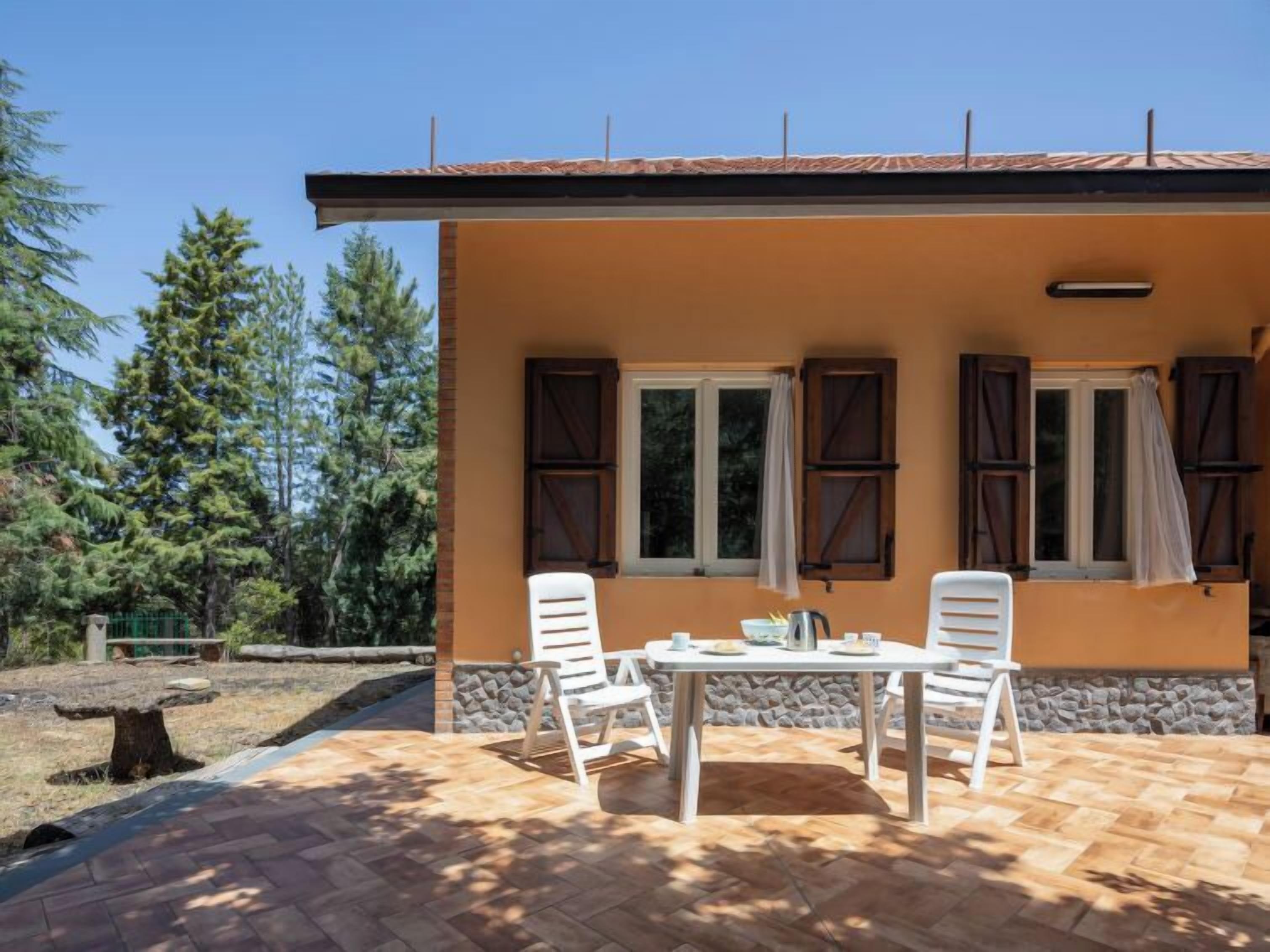 Un edificio con due finestre, un muro in pietra e un patio con due sedie bianche e un tavolo.
