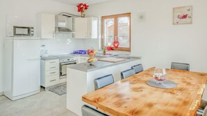 A modern kitchen with white cabinets, a wooden dining table, and a window with a heart-shaped decoration.