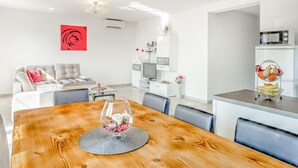 A modern living room with a dining table, sofa, TV, and kitchen area.