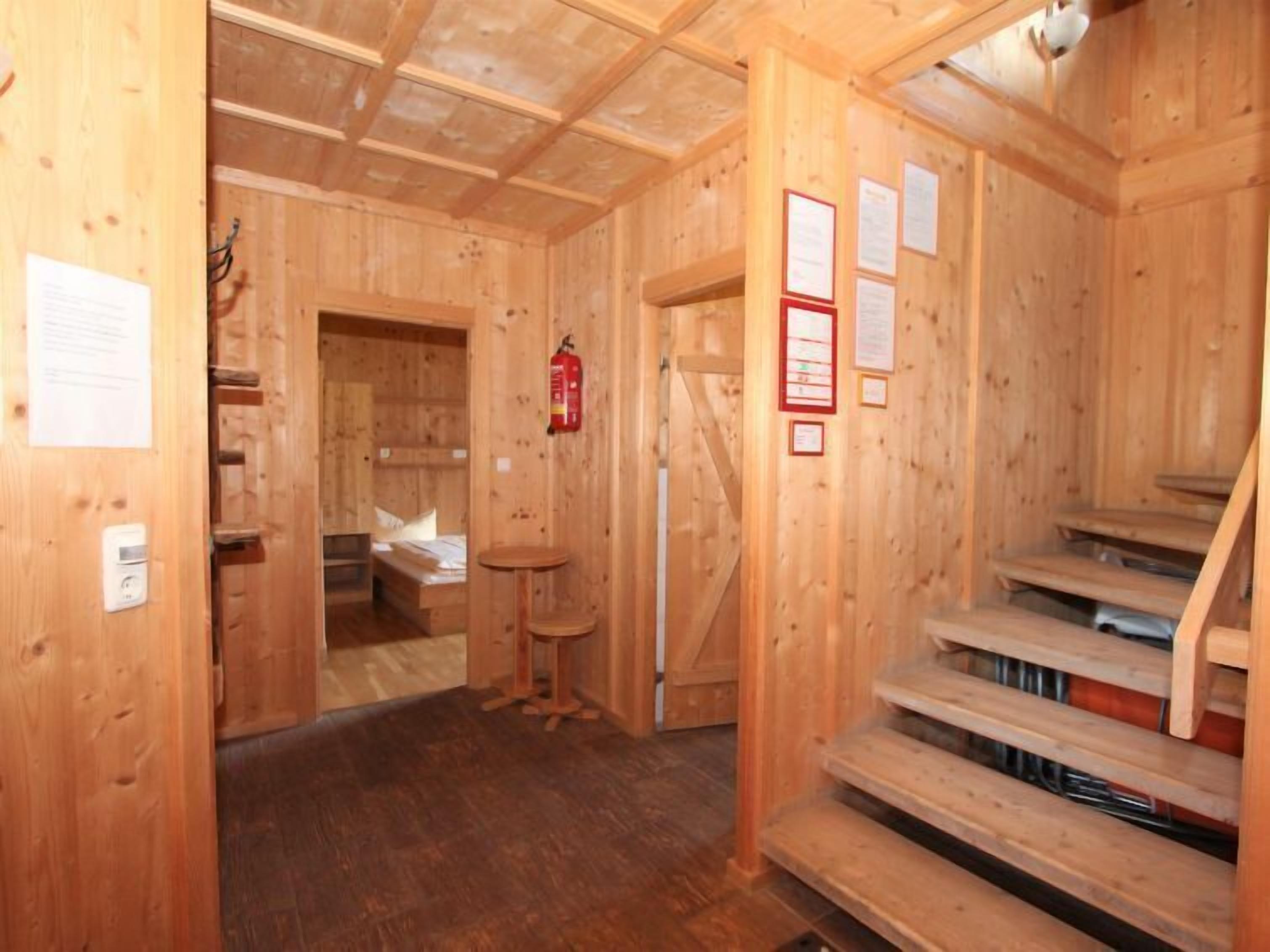 Interior de una cabaña de madera con escalera, una mesa pequeña y una cama.