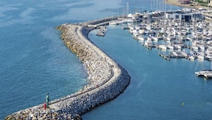 A coastal marina with boats docked, a rocky breakwater, and a statue on a small island. - Villa il Pellicano by Interhome (San Vincenzo)