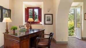 A room with a wooden desk, two lamps, a chair, a window with red shutters, and a framed picture on the wall. - La Forra by Interhome (Vicchio)