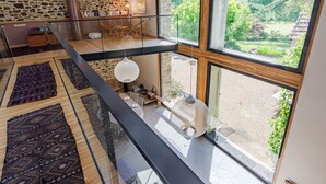 Un loft spacieux avec un mur en pierre, une mezzanine et de grandes fenêtres donnant sur le jardin.