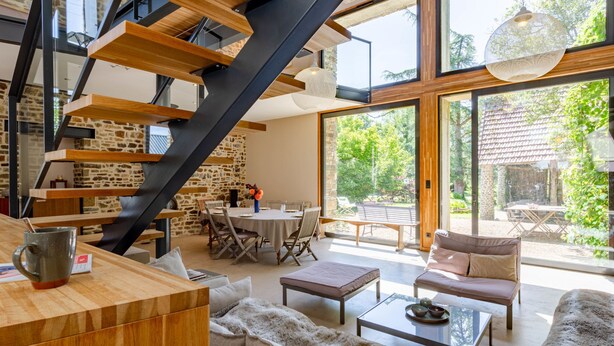 Un vaste espace de vie comprenant un escalier en bois, une table à manger et un ensemble de canapés.