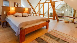 Une chambre avec une structure de plafond en bois, un lit doté d’une tête de lit et une vue sur un mur en pierre et un escalier.
