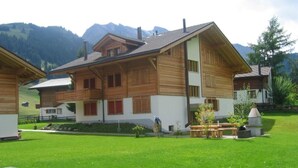 A wooden chalet with a sloped roof, multiple windows, and a well-maintained lawn in a mountainous area. - Am Gilsbach 2 by Interhome (Adelboden)