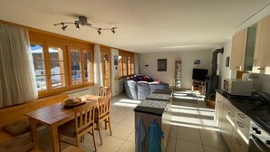 A spacious living area with a dining table, chairs, a sofa, and a kitchen with a stove and cabinets. - Am Gilsbach 2 by Interhome (Adelboden)