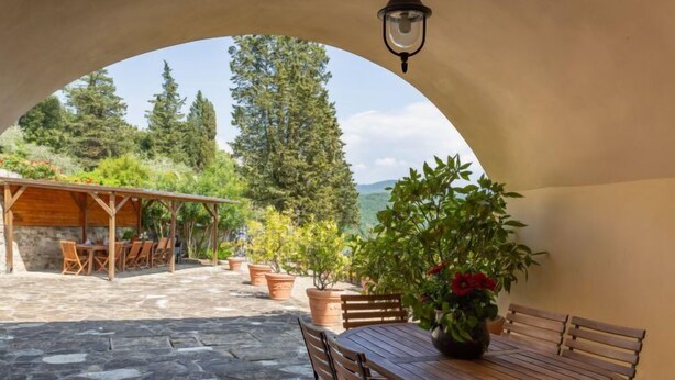 An outdoor patio with a wooden table and chairs, surrounded by potted plants and a stone floor. - Villa Monteloro by Interhome (Florence)