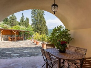 An outdoor patio with a wooden table and chairs, surrounded by potted plants and a stone floor. - Villa Monteloro by Interhome (Florence)