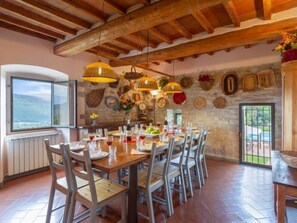 A dining area with a stone wall, wooden ceiling beams, and a large window overlooking a scenic landscape.