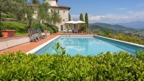 A pool with lounge chairs and a gazebo, surrounded by greenery and a stone building with a view of the hills. - Villa Monteloro by Interhome (Florence)
