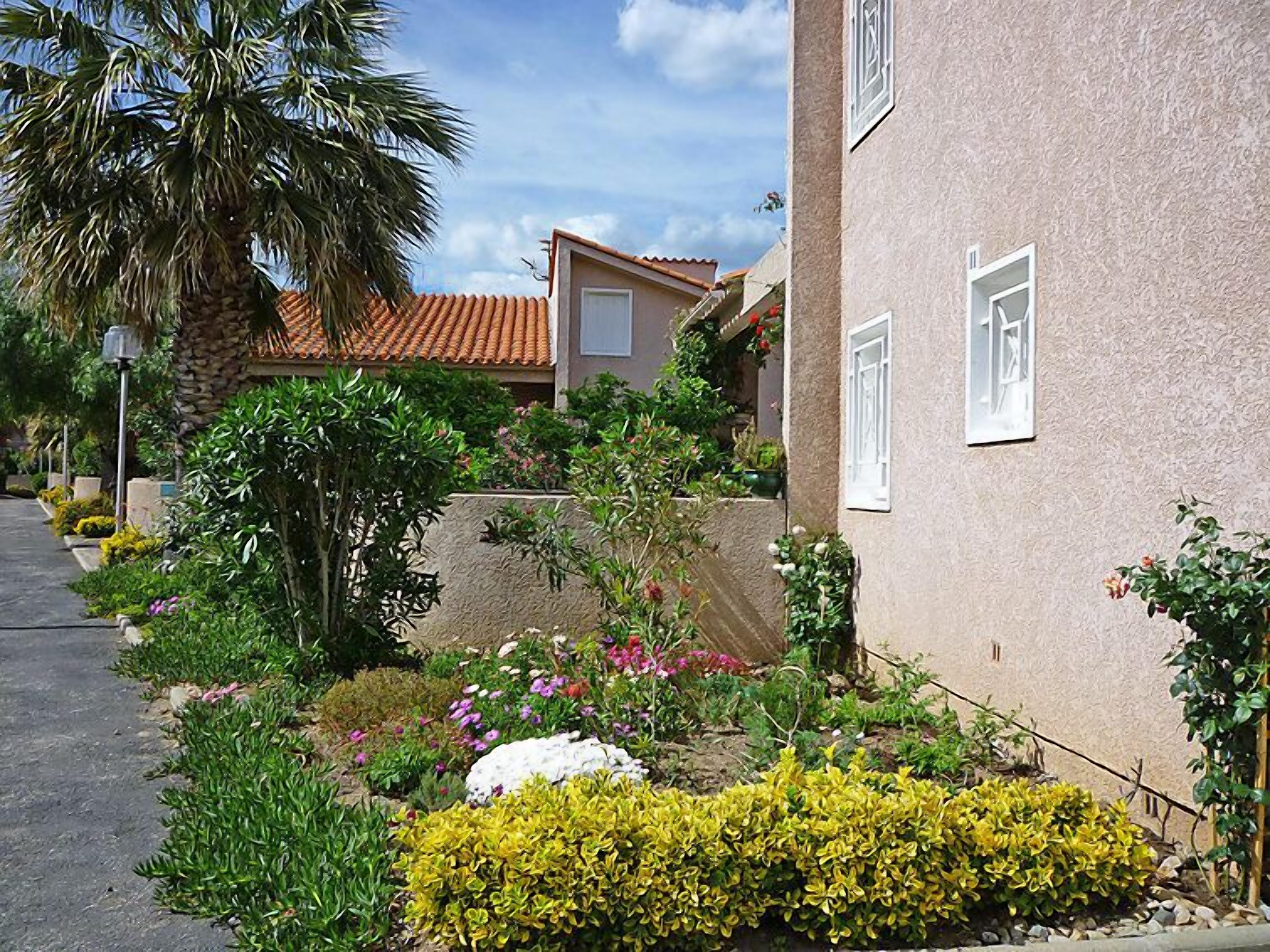 A residential building with a stucco exterior, a tiled roof, and a small balcony with potted plants.