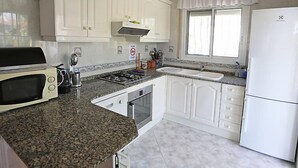 Een keuken met witte kasten, een gasfornuis, een magnetron, een spoelbak en een koelkast.