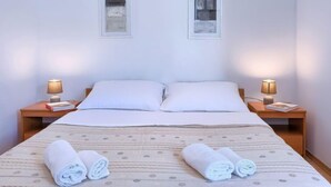 A neatly made bed with white linens and two rolled towels on the bed. There are two bedside tables with lamps on either side of the bed. - Apartment Nika by Interhome (Umag)