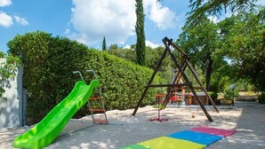 Un parque infantil con un tobogán verde, columpios y una zona de juegos suave con paneles de espuma.