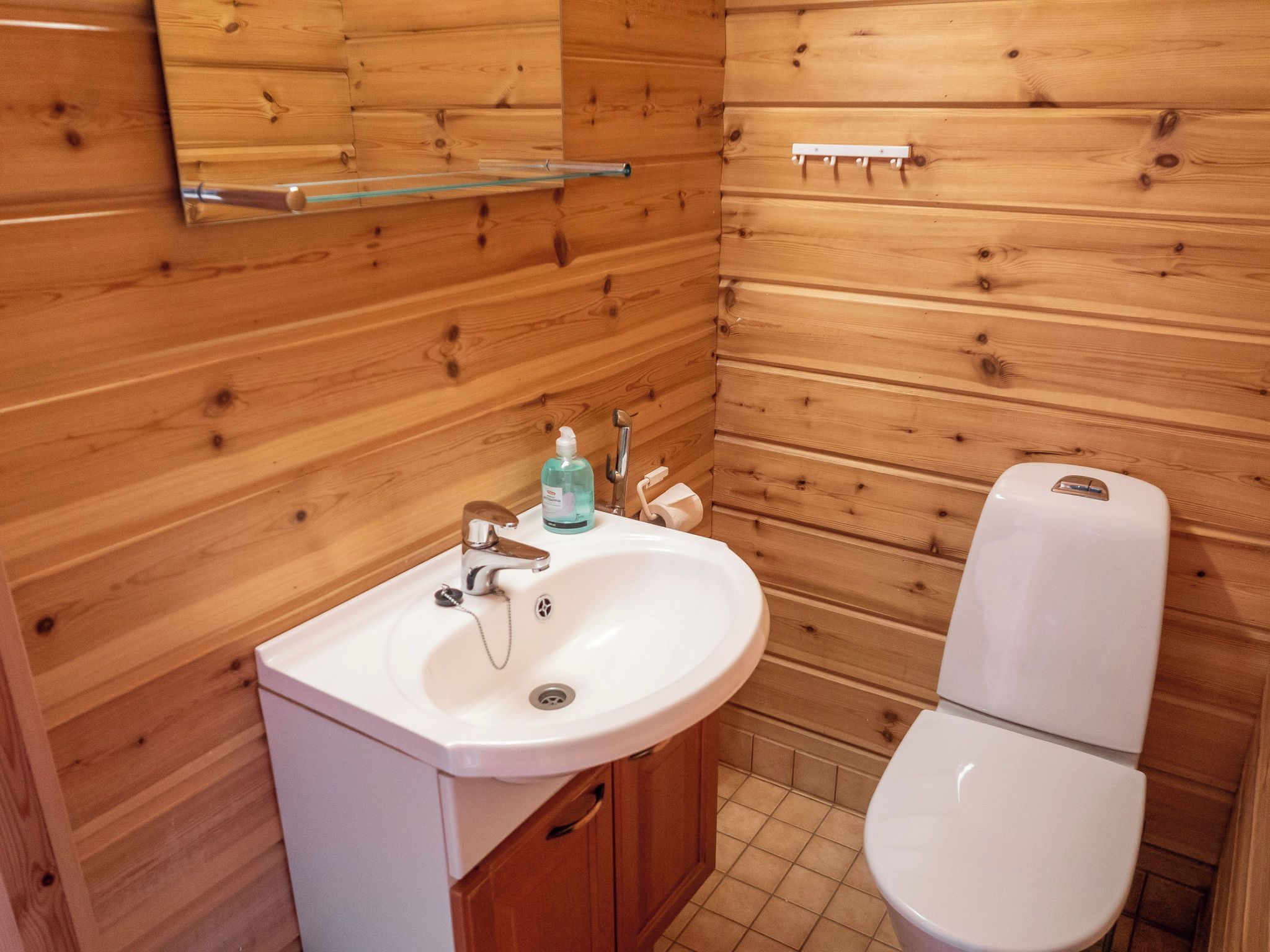 Un baño con paneles de madera, un lavamanos blanco, un grifo y un inodoro.