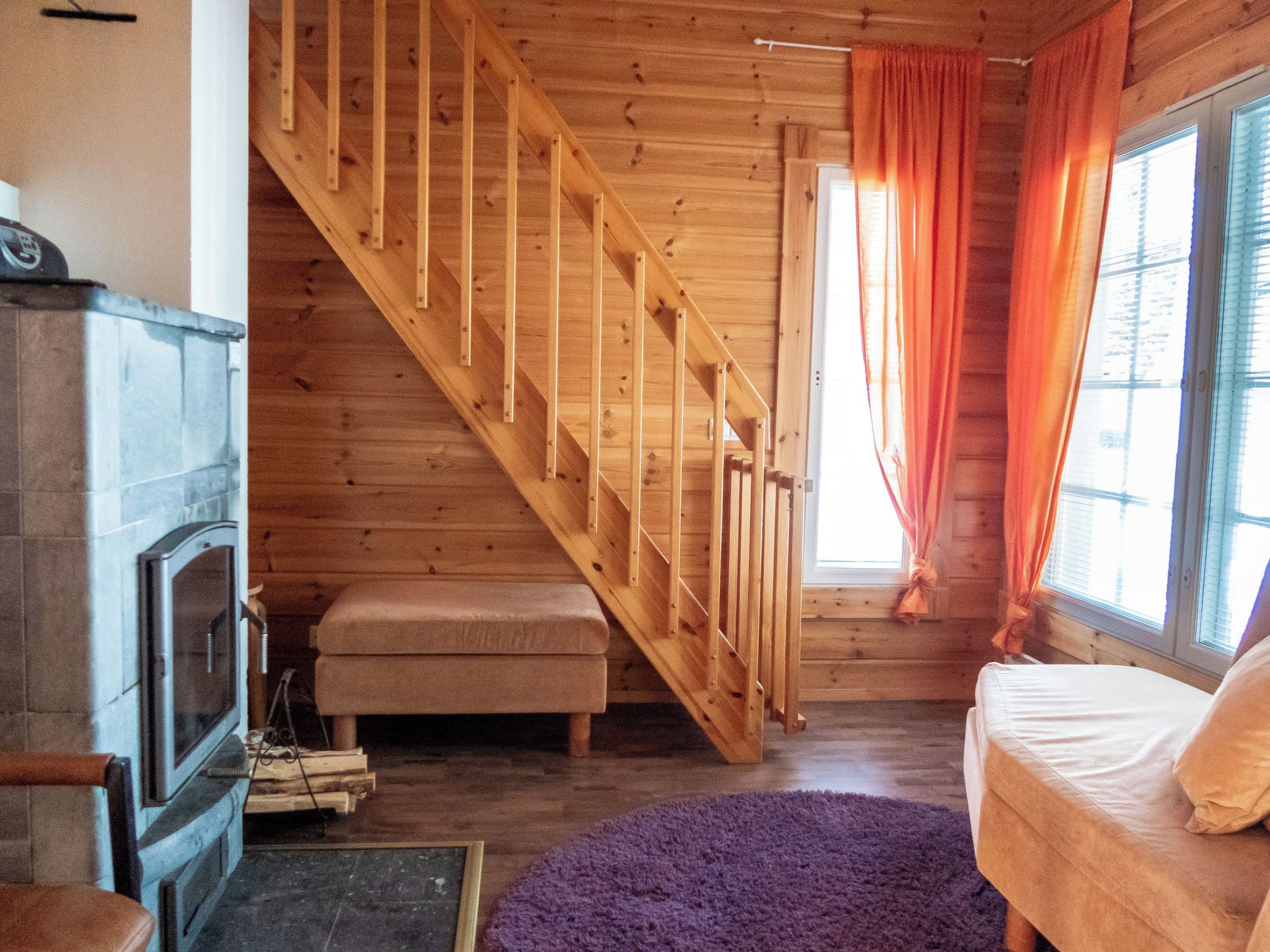 Un escalier en bois mène à une chambre mansardée, où se trouvent un lit et une fenêtre avec des rideaux.