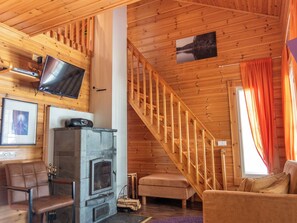A wooden interior with a fireplace, a television mounted on the wall, and a staircase. - Klz 1. akvamariini by Interhome (Sotkamo)