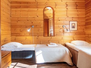 Une chambre dans un chalet en bois, avec deux lits, un miroir, un tableau accroché au mur et une lampe sur pied.