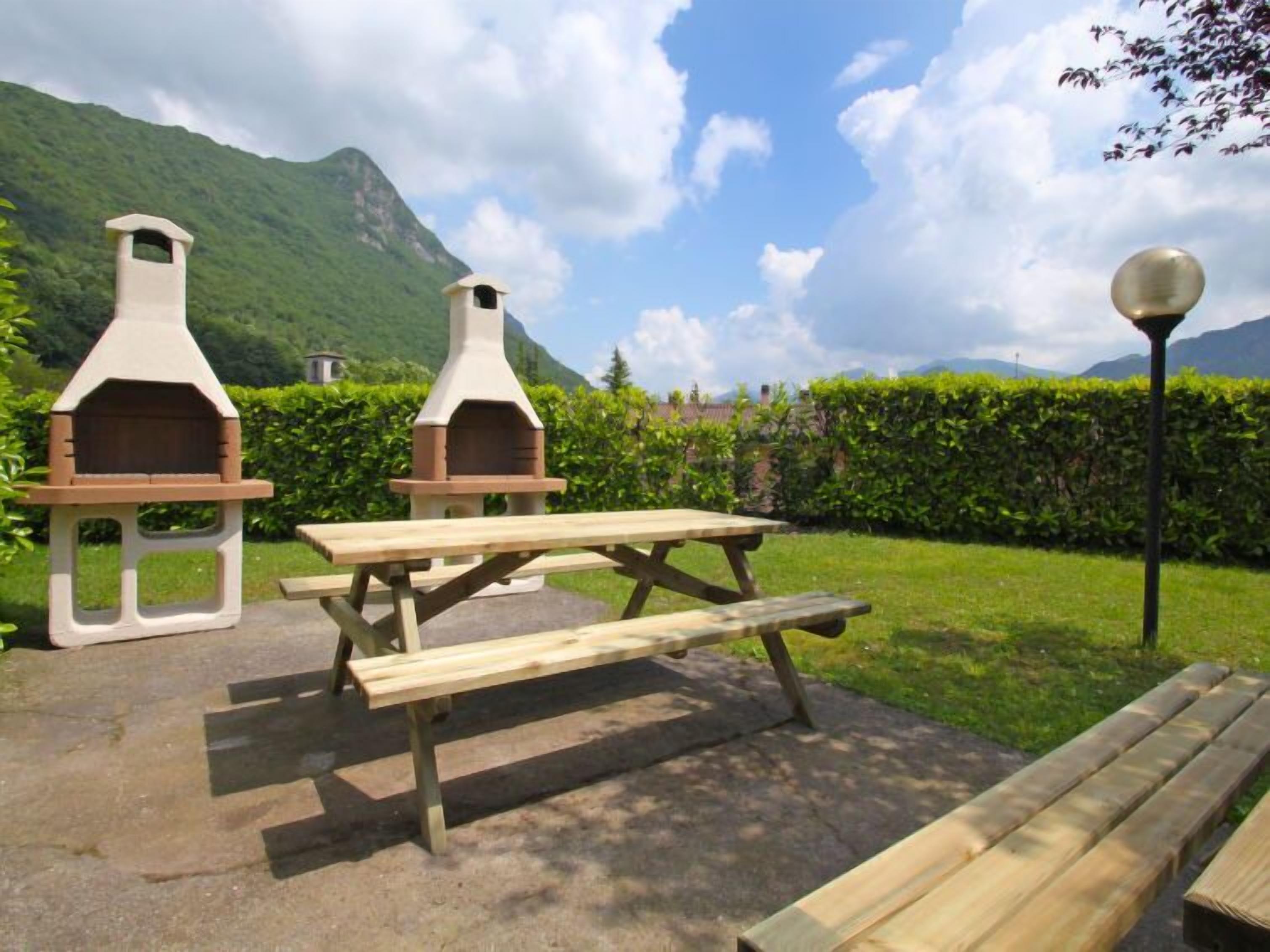 An outdoor patio with two stone barbecue grills, a wooden picnic table, and a lamp post.