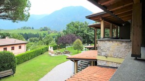 Un escalier mène à un espace extérieur abrité, doté d’un mur en pierre, d’une pelouse et offrant une vue sur les montagnes en arrière-plan.