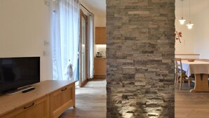 Un salon moderne doté d’un téléviseur à écran plat, de meubles en bois, d’un mur d’accent en pierre et d’un coin repas avec une table et des chaises.