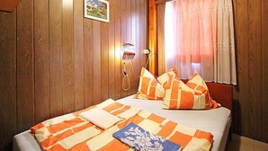 Un dormitorio con paredes de madera, una cama con ropa de cama naranja y blanca, un cuadro en la pared y una ventana con cortinas.