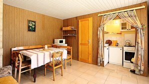 Una habitación compacta con una mesa de madera, microondas, pequeña cocina con estufa y hervidor, y una puerta que da a otra habitación.