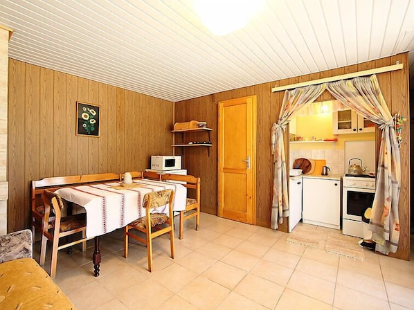 Una habitación compacta con una mesa de madera, microondas, pequeña cocina con estufa y hervidor, y una puerta que da a otra habitación.