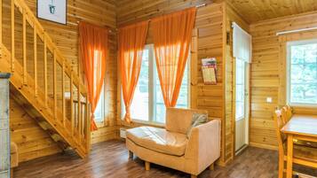 Interior de una cabaña de madera con sofá, mesa de comedor y una escalera.