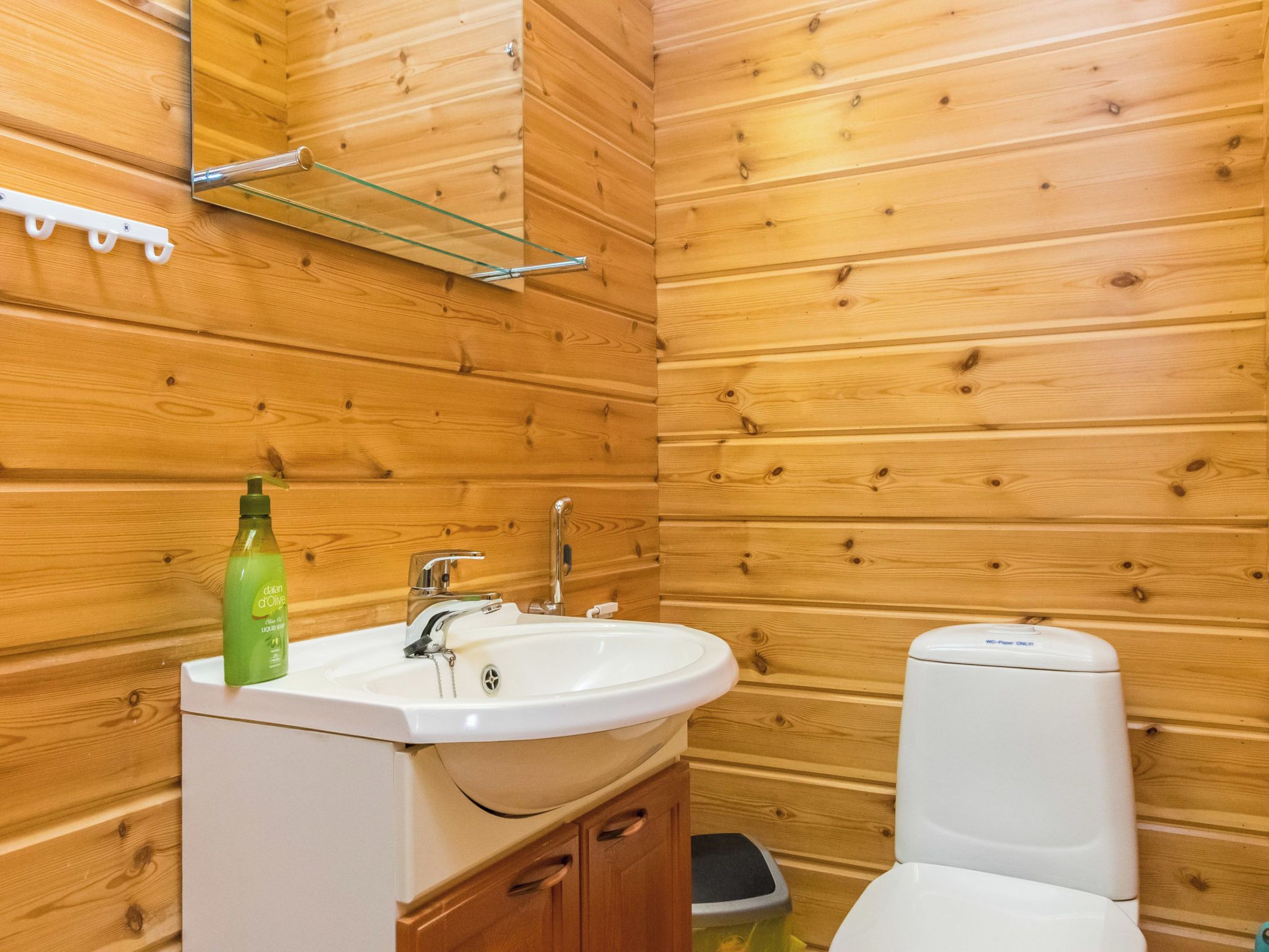 Un bagno con rivestimenti in legno, un lavandino bianco, un water e una bottiglia verde di olio d'oliva.