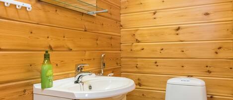 Un bagno con rivestimenti in legno, un lavandino bianco, un water e una bottiglia verde di olio d'oliva.