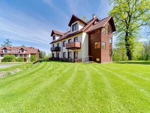 Une maison à deux étages avec une pelouse bien entretenue, une terrasse en bois et un grand arbre en arrière-plan.