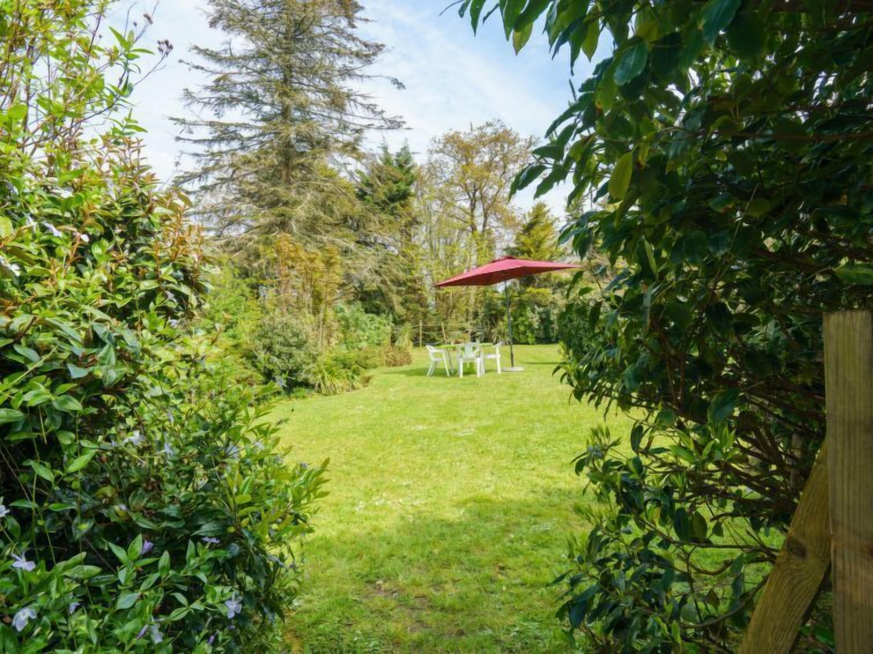 A lush garden with a red umbrella, white chairs, and a wooden fence.