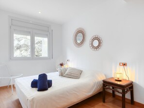 Ein Schlafzimmer mit einem Bett, zwei Wandspiegeln, einem Nachttisch mit Lampe, einem Sessel und einem Fenster mit Blick auf Felsen.