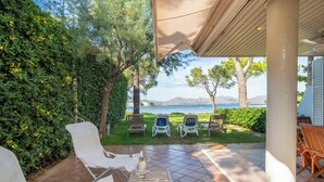 An outdoor patio with white lounge chairs, a wooden table, and a view of the sea. - Es Clot by Interhome (Alcúdia)
