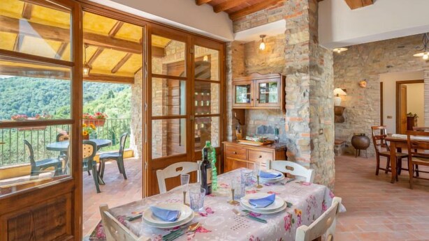 A dining area with a table set for four, stone walls, wooden beams, and a view of greenery outside. - Dante 2 by Interhome (Lucca)
