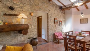 A rustic interior with exposed stone walls, wooden beams, a dining area with a table and chairs, a sofa, and a hanging lamp. - Dante 2 by Interhome (Lucca)
