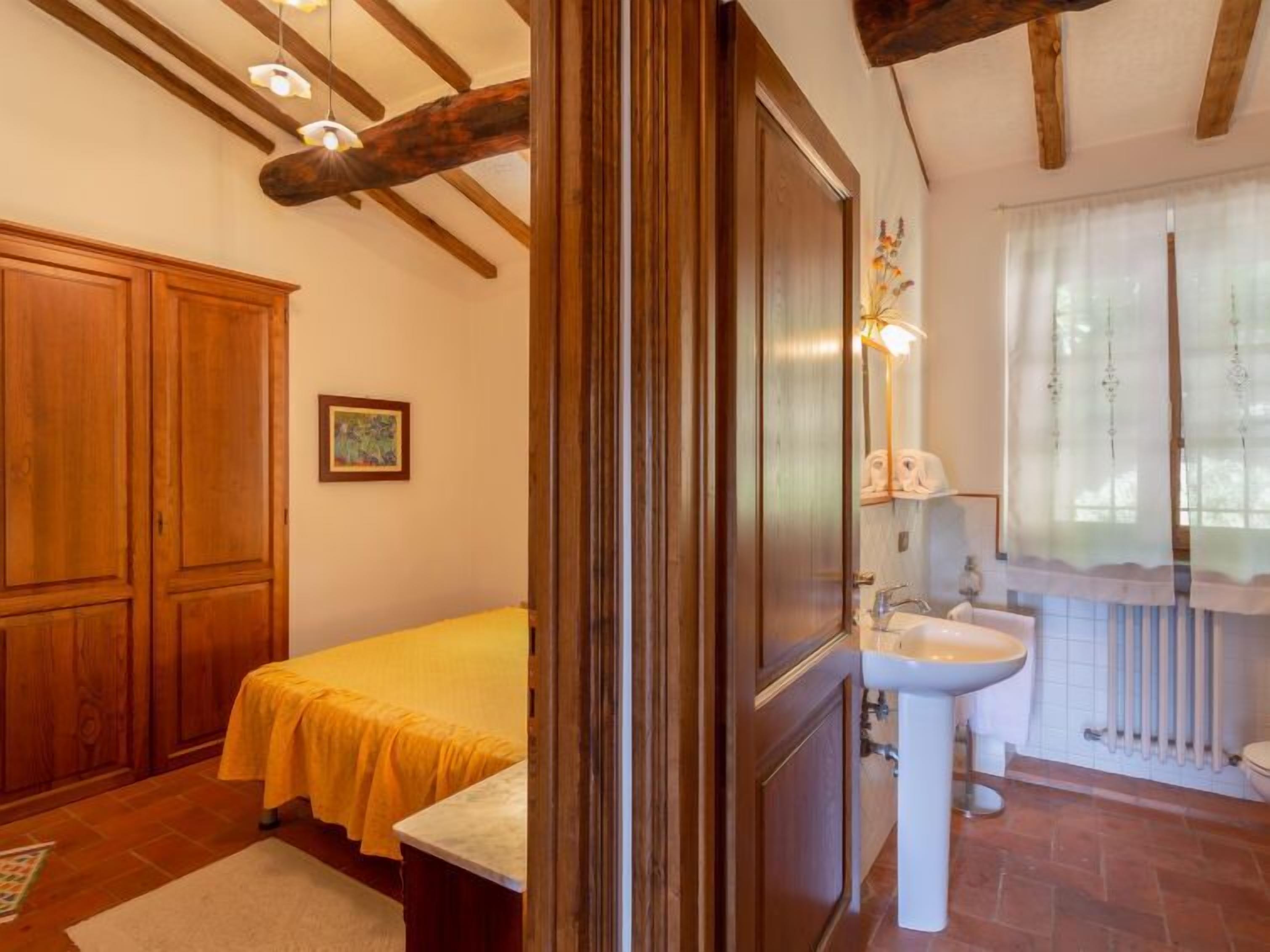 Un dormitorio con cama, armario de madera y baño con lavabo y ventana.