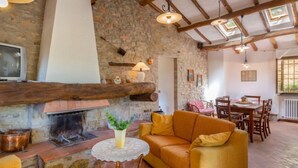 A cozy living room with a stone fireplace, wooden beams, and a dining area with a table and chairs. - Dante 2 by Interhome (Lucca)