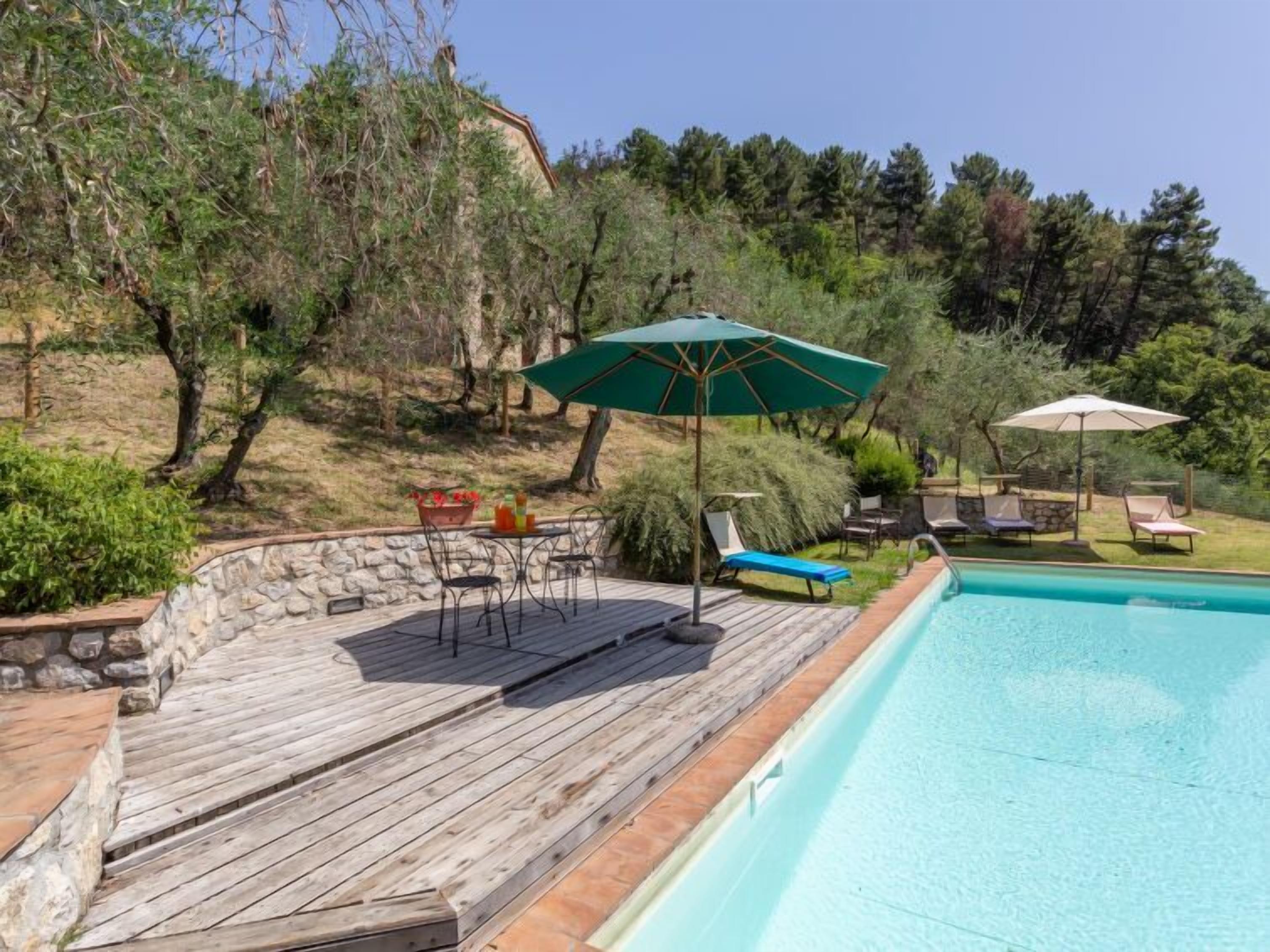 A wooden deck with a pool, outdoor furniture, and a stone wall.