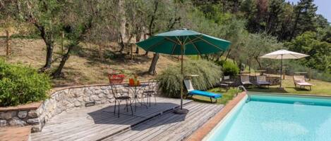 A wooden deck with a pool, outdoor furniture, and a stone wall.