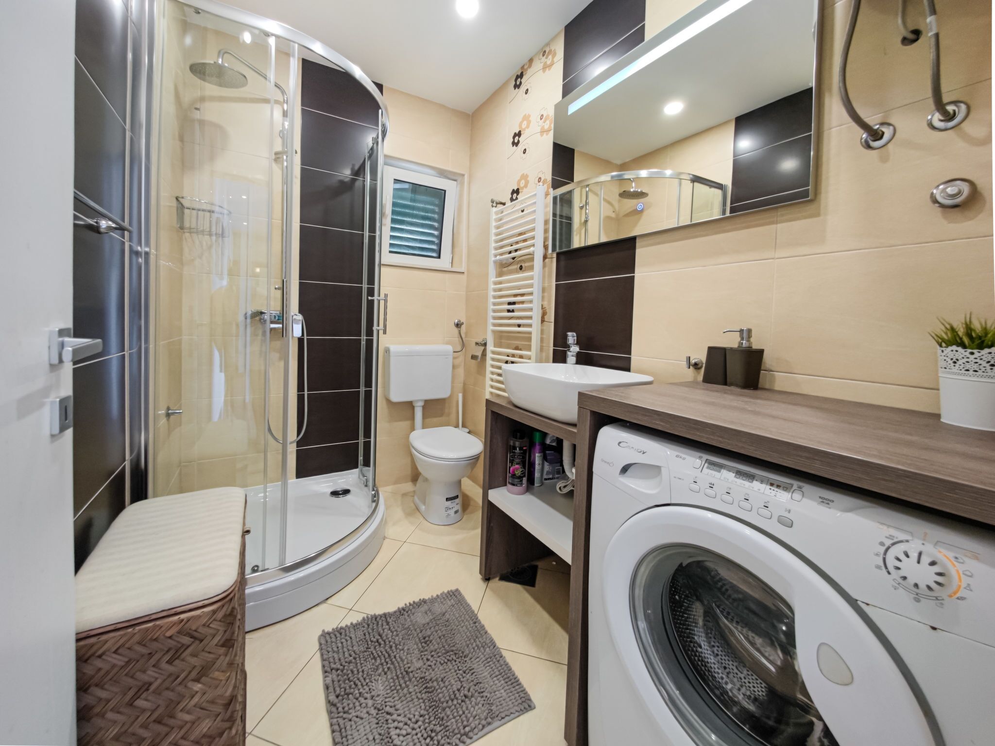 A modern bathroom with a glass-enclosed shower, a toilet, a sink, and a washing machine.