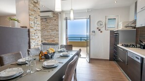 Una cocina moderna con comedor, pared de piedra y vista al mar.