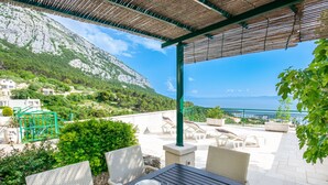 Una terraza con mesa lista para comer, con vistas a un paisaje montañoso y al mar.