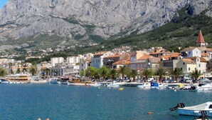 Un pueblo costero con edificios, un puerto deportivo y montañas al fondo.