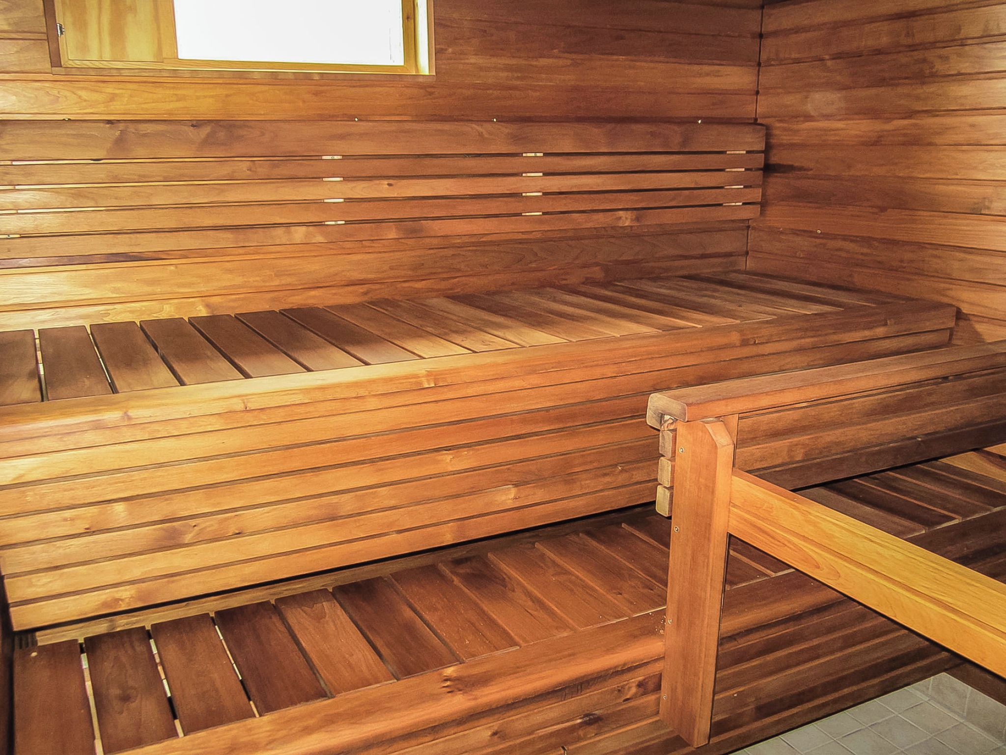 Een houten sauna bank met een lattenstructuur, een houten frame en een raam erboven.