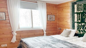Dormitorio con paneles de madera, cama, cortinas blancas y un cuadro en la pared.