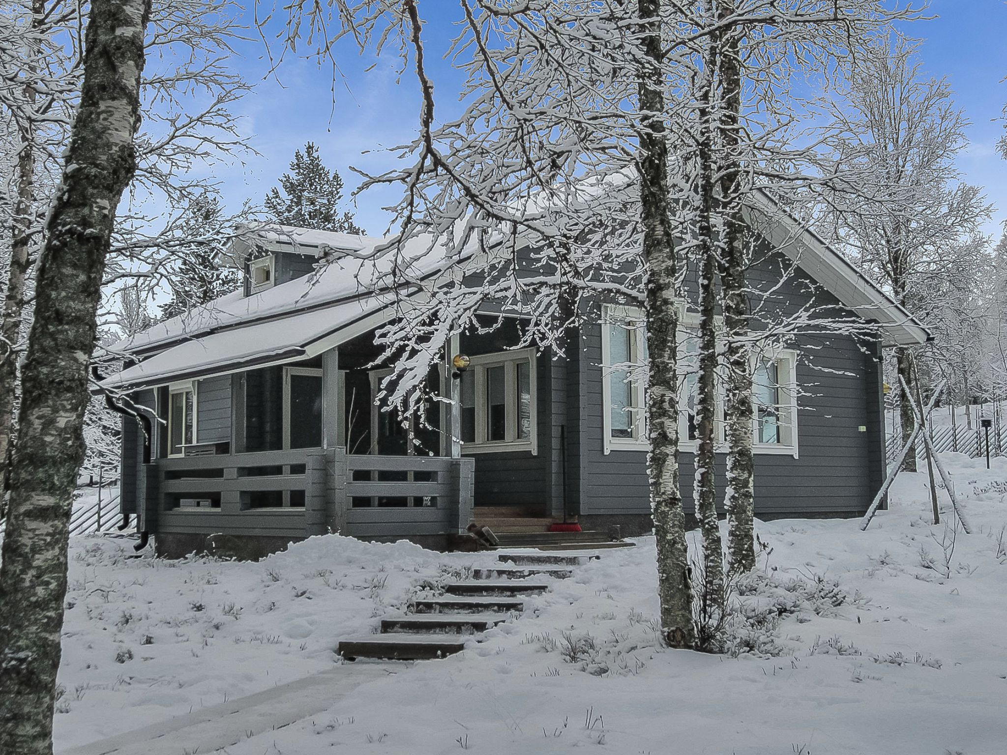 A cabin with a wooden porch, surrounded by snow-covered trees.